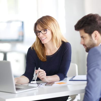 Man and woman in an office look at laptop screen together.