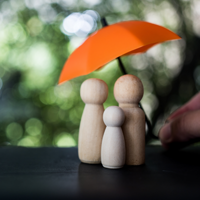 Three wooden cutouts meant to resemble people on a table with a small orange umbrella over them